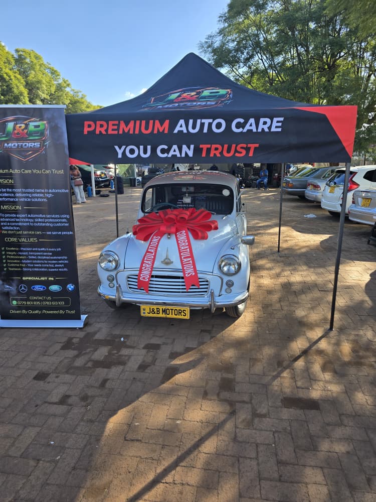 The Morris Minor parked under the J&B Motors marquee, ribbon hidden, waiting for the reveal
